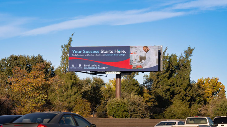 Billboard for American River College against a backdrop of trees